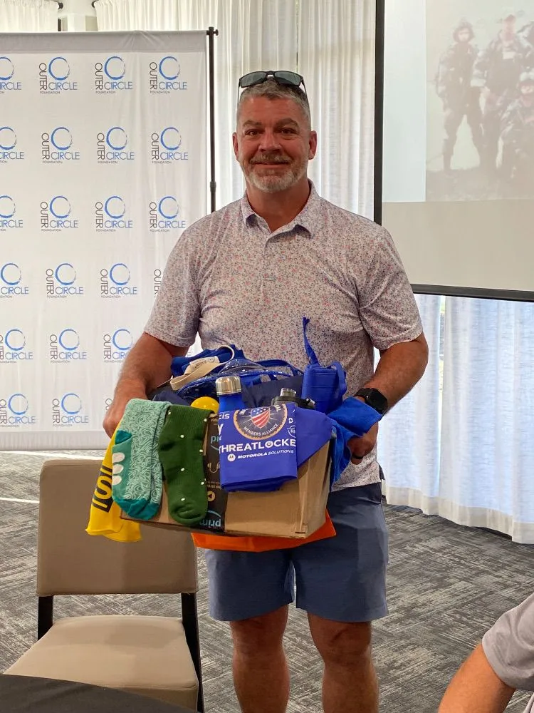 Golf outing guest displaying a raffle or auction prize basket he won at an Outer Circle Foundation event